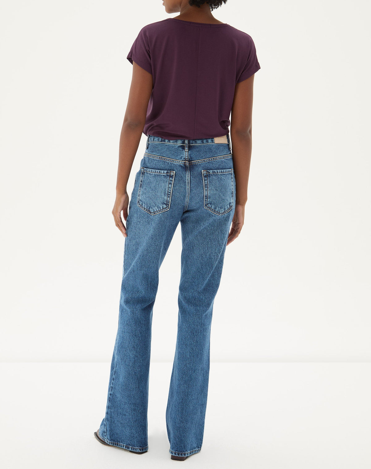 Vista traseira da calça jeans flare azul médio com blusa roxa.