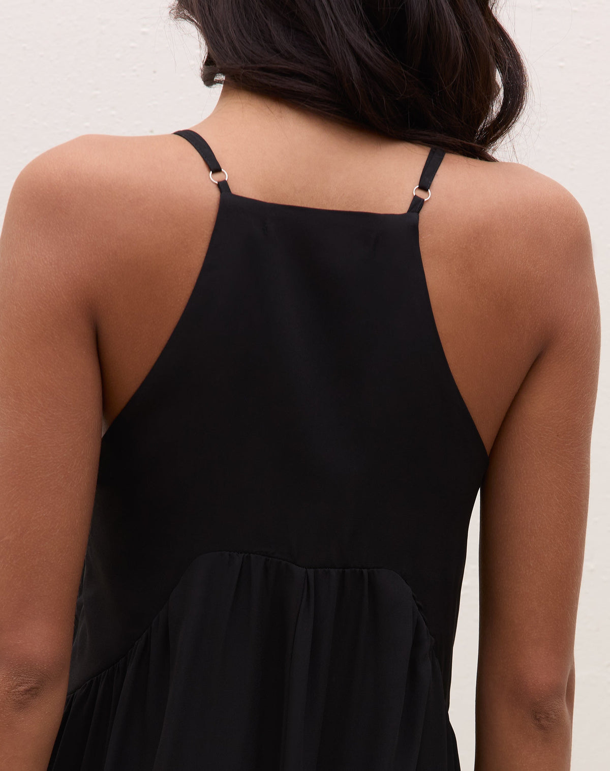Visão traseira do vestido maxi preto mostrando costas regata, alças finas ajustáveis e saia longa com babado na barra