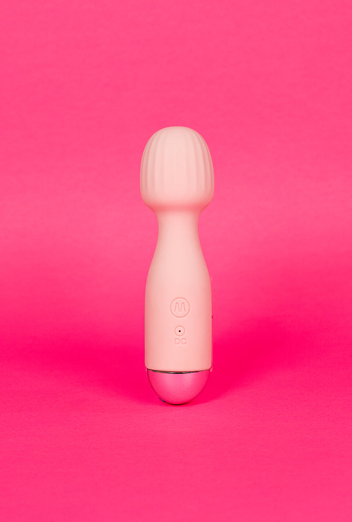 Vibrador varinha magica MINA recarregável em silicone rosa sobre fundo pink.