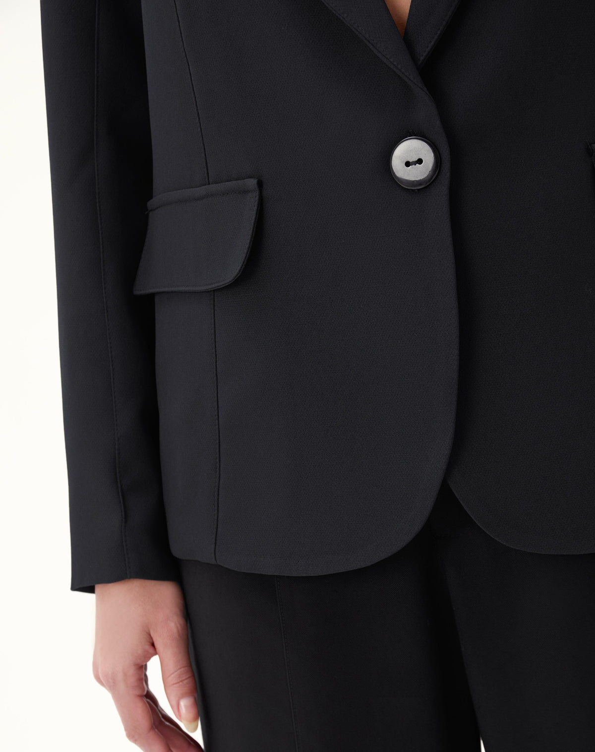 Detalhe do bolso com aba e botão do blazer preto.
