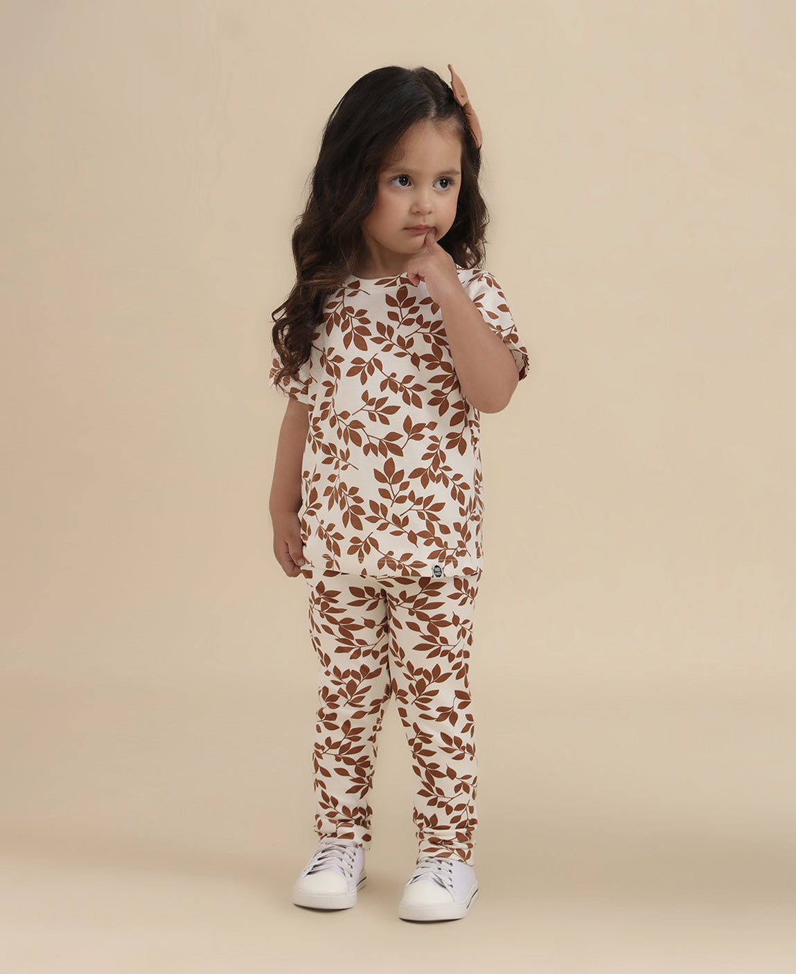 Detalhe da estampa Laurel folhagem louro na Calça Legging Reta MiniMalista. Folhas de louro estilizadas allover em caramelo dourado sobre fundo neutro. Legging infantil 100% algodão unissex, cós sem cadarço.