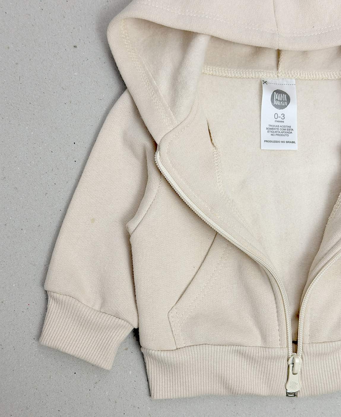 Casaco Infantil Bege Claro Peluciado MiniMalista Baby — vista lateral mostrando o corte folgado proposital, feito pra usar como terceira camada sobre body ou camiseta canelada. Cobre-zíper interno protege o queixo. Unissex, do bebê aos 5-6 anos.