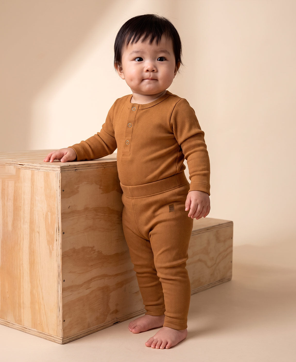 Calça Slim Canelada Bebê Liso Goldie MiniMalista Baby — cós elástico wide sem cadarço, etiqueta de couro caramelo no hip, malha canelada caramelo tostado 100% algodão fitted.